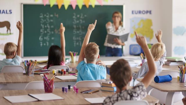 Niños en una clase subiendo la mano para responder a la profesora